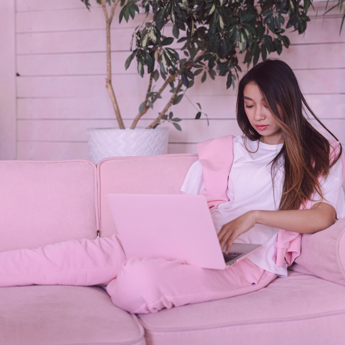 Woman learning how to pitch to brands on a pink couch with laptop.