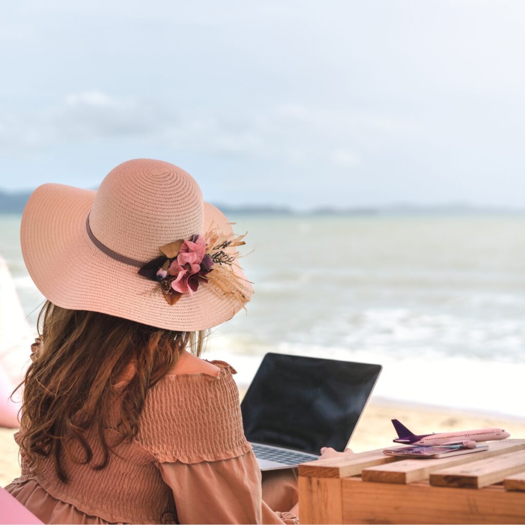 Woman on a beach with a laptop exploring travel blog niche ideas.