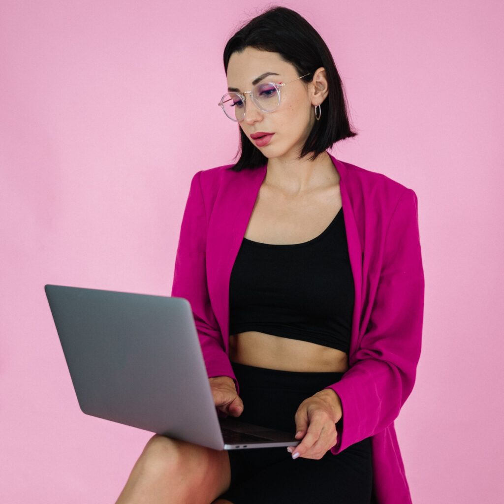 Woman in a pink blazer reviewing a blogger collaboration agreement on a laptop.