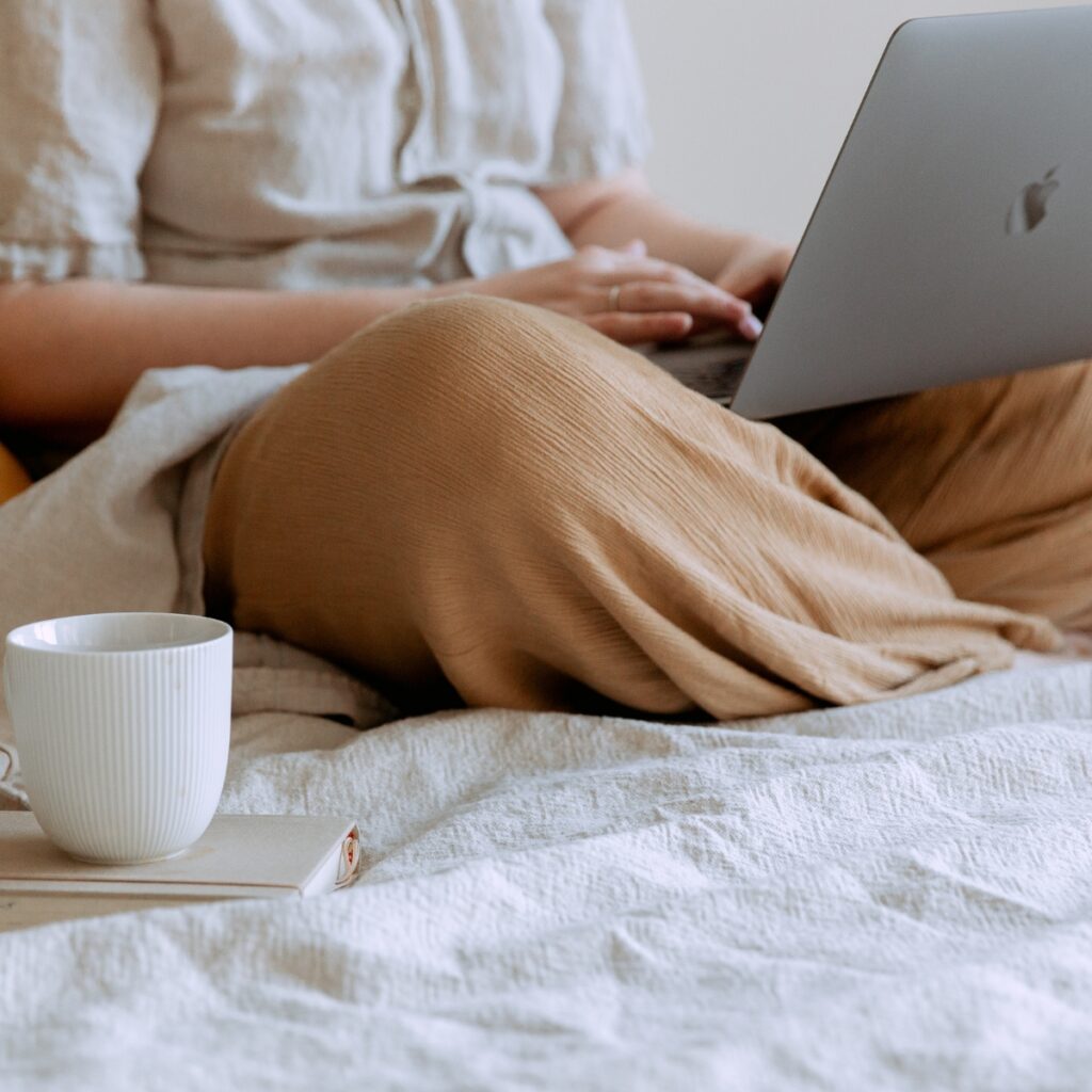 Woman on a laptop in bed with a coffee mug.